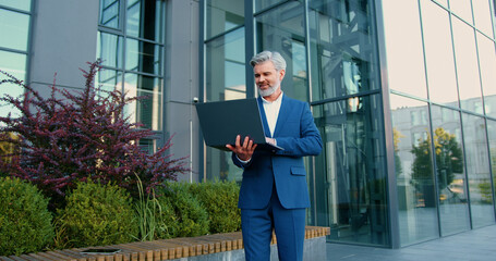 Handsome older man entrepreneur using laptop remotely computer for online business. Focused mature...