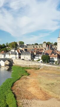 Scenic view of La Charite sur Loire with traditional houses, a stone bridge, and the Loire riverbank under a bright sky. Picturesque French village atmosphere.