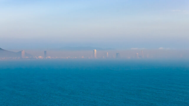 Aerial view of the distant skyline shrouded in a soft, hazy mist rising from the tranquil sea, Bai Xep Beach, Binh Dinh, Vietnam.