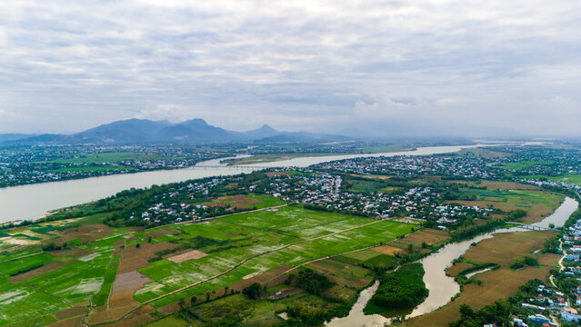 Aerial view of a river winding through verdant rice paddies and tranquil villages under a soft sky, Hoi An, Quang Nam, Vietnam.
