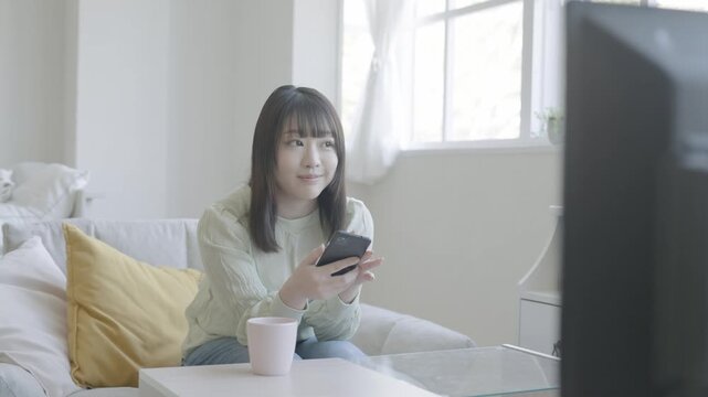 テレビを見ながらスマホを見る女性