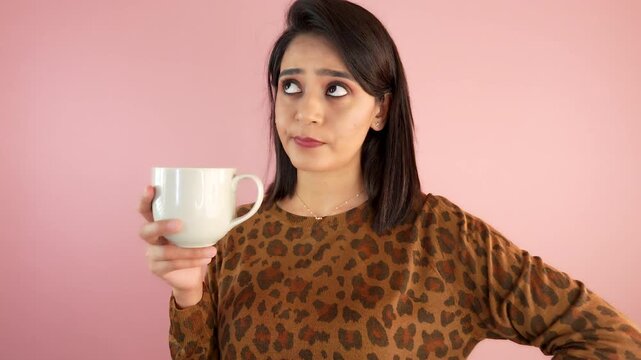 Close up of confused thoughtful young Asian woman lady holding coffee cup thinks ideas choice doubt feels confusion, isolated against light pink studio background.