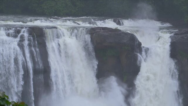 slow motion video of water fall rushing water over dark rocks. White foam crashes against stone with force and energy. Nature's raw power fills the frame. Ideal for backgrounds showing energy, Kerala