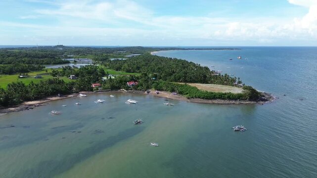 Cinematic aerial drone footage of small fishing boats anchored near tropical coastline with rice fields and lush green nature in the background Carles Iloilo Philippines peaceful landscape