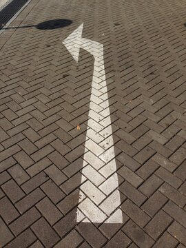 white directional arrow painted on brick pavement