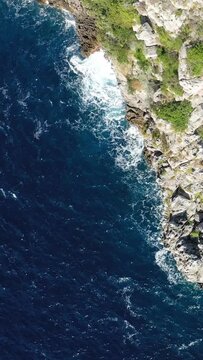 Drone shot of rugged cliffs and deep blue sea at Capo di Conca, Italy. Dramatic waves crash against the rocky shoreline with lush greenery above.