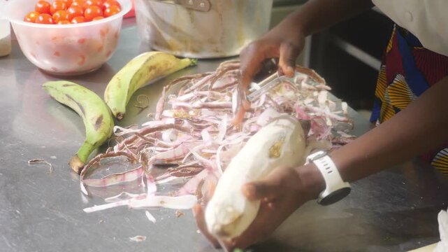 Close view of chef peeling cassava root with knife on metal work surface during preparation of fresh ingredients in a professional kitchen.