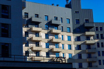 Modern apartment block with geometric balconies. Bold angles contrasted against clear blue sky. Sunlight casts sharp shadows across building surfaces. Ideal for urban design, architecture © Алексей Петров