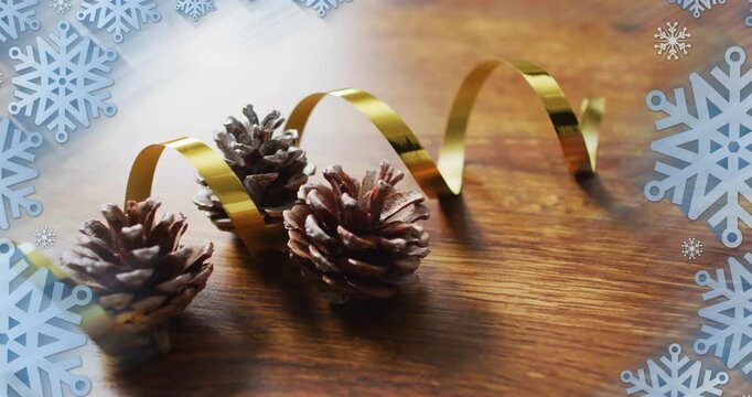 Animation of christmas decorations with pine cones over snowflakes on wooden background