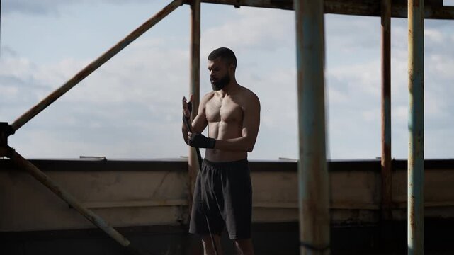Young Black male with muscular body wrapping hands for boxing workout on rooftop