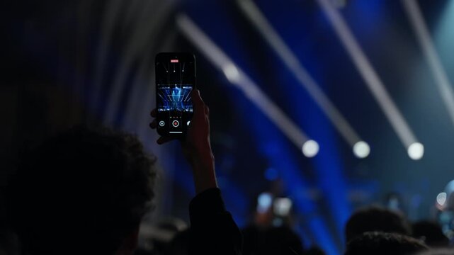 A dynamic video showcasing a person in a silhouetted crowd at a live concert, holding a smartphone to record the blue-lit stage