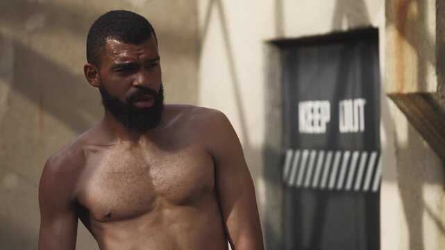 Exhausted Black male boxer wiping sweat after intense training on empty rooftop