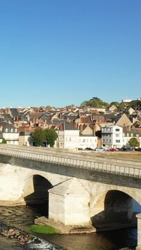 Scenic view of a historic stone bridge crossing the river with traditional rooftops and houses in La Charite sur Loire, France, under a clear blue sky.
