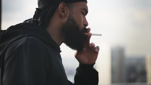 Young African American man in durag lighting a cigarette on rooftop, relaxation