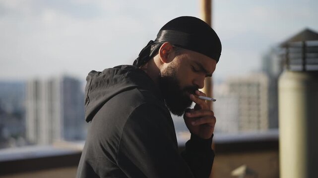 Young man in a hoodie smoking cigarette on empty rooftop, bad boy image