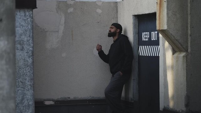 Bearded African American man in a hoodie smoking cigarette near rooftop entrance