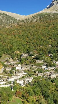 Aerial view of a picturesque stone village nestled among lush green mountains in Papingo, Greece, under a clear blue sky.