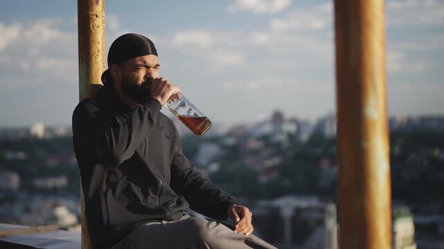 African American man drinks liquor on the edge of city rooftop, depression