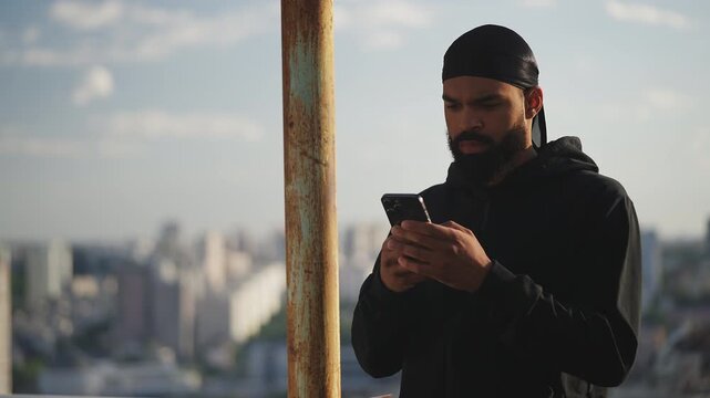 Black man in a durag typing on cellphone on rooftop, setting up a meeting