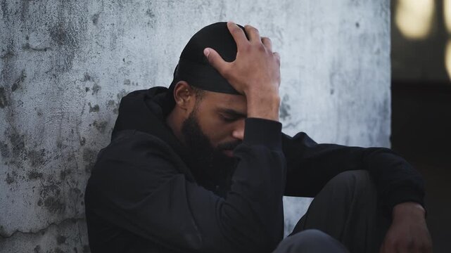 Upset Black man in durag sitting on rooftop, holding his head in a tense moment