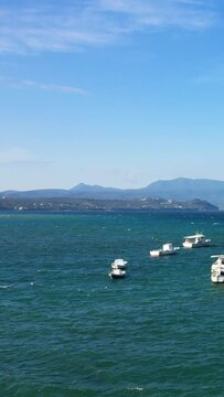 Small fishing boats floating on the turquoise waters near Koroni, Greece, with distant mountains under a clear blue sky. Peaceful maritime scene ideal for travel and relaxation concepts.