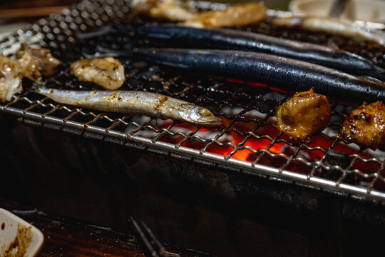 Lanyu, Taiwan - June 23, 2025: Fresh Pacific saury grilling over glowing charcoal on a BBQ rack.
