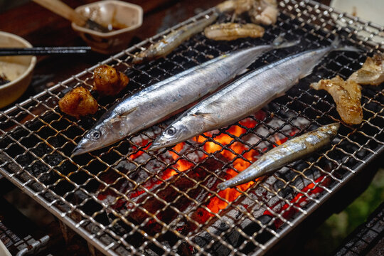 Lanyu, Taiwan - June 23, 2025: Fresh Pacific saury grilling over glowing charcoal on a BBQ rack.