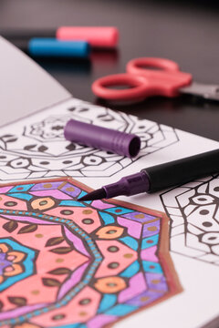 Adult coloring book with a partially colored mandala and markers