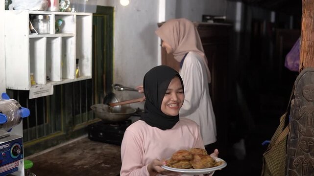 Asian muslim women in rustic kitchen preparing homemade snacks, hijab mentor guiding young apprentice carrying golden fried
