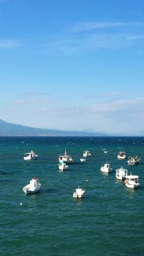 Small fishing boats float on the clear turquoise waters off the coast of Koroni, Greece, with distant mountains under a bright blue sky.