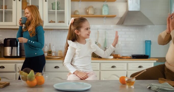 Grandfather and granddaughter playing at kitchen table while grandmother and mother talk. Multigenerational family, happy bonding, love and joyful home lifestyle moment.