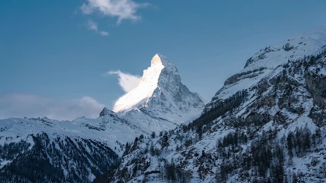 Timelapse shows Matterhorn above Zermatt in Valais as clouds race by, alpenglow lights the summit, and long shadows move over snow ridges and sparse larch slopes.