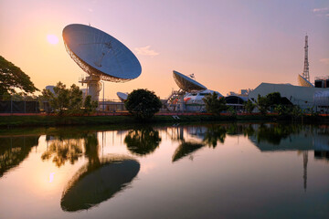 Obraz premium Large satellite dish antenna station by pond at dawn, Bangkok