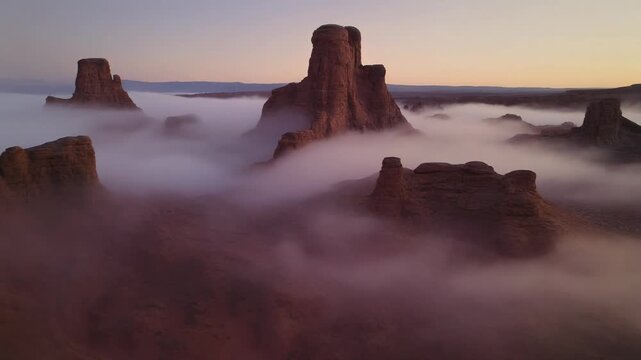 Misty sunrise over rugged rock formations in a desert landscape with fog rolling in