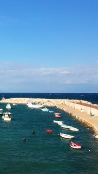 Small fishing boats float in the turquoise waters of Koroni harbor, with a stone breakwater and clear blue sky in the background. Peaceful coastal scene ideal for travel and lifestyle concepts.