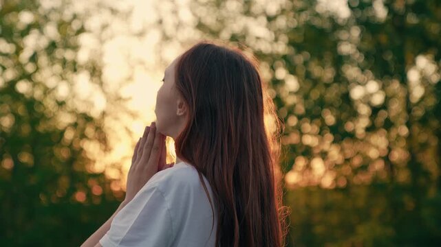 Relaxing meditation in nature. Christian woman prays outdoors sunrise. Faith in God. Beautiful girl in park in sun prays to family children. Asking for forgiveness. Hope. Woman in nature. Close-up