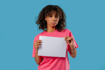 Serious woman holding blank a4 white sheet of paper on blue studio background.Protest, complaint,...