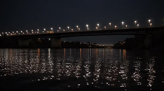 Nighttime view of a city bridge spanning dark water, illuminated by numerous streetlights