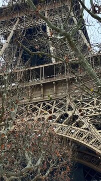 Close-up view of the Eiffel Tower in Paris, France, highlighting its intricate iron architecture and design. Bare trees indicate late autumn or early spring, capturing a classic travel destination 