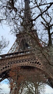 Close-up view of the Eiffel Tower in Paris, France, highlighting its intricate iron architecture and design. Bare trees indicate late autumn or early spring, capturing a classic travel destination 