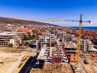 Naklejka premium Building site in coastal town with crane and construction workers during midday sunshine