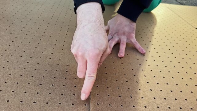 Hands are focused on aligning sections of perforated board on ground outside in bright natural light.