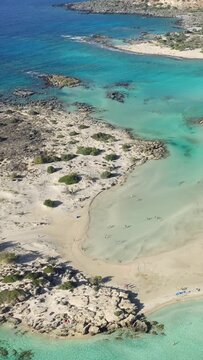 Stunning aerial view of Elafonisi beach with turquoise waters, sandy shores, and rocky coastline in Crete, Greece. The clear shallow lagoon and natural landscape create a serene Mediterranean scene.