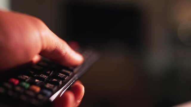 Close-Up of Hand Using a TV Remote Control: A Concept of Media Consumption, Channel Surfing, and Home Entertainment