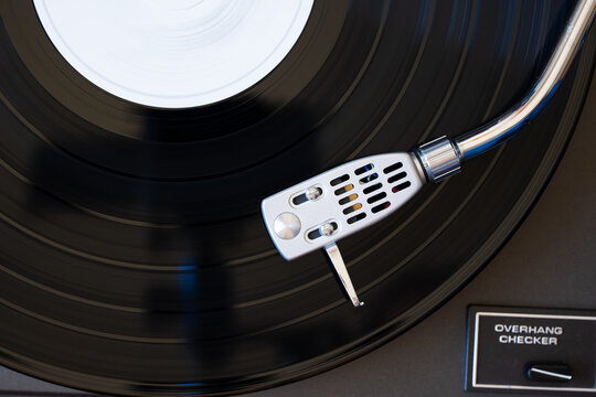 Turntable headshell and needle on a spinnig vinyl record. Top down, close up view, no people