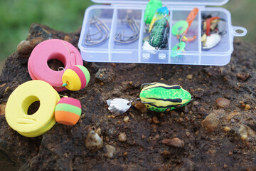 Fishing tackle set with colorful lures, hooks, floats and foam line spools arranged on rock near water, showcasing outdoor angling gear and preparation for freshwater fishing activity. © Sanhanat