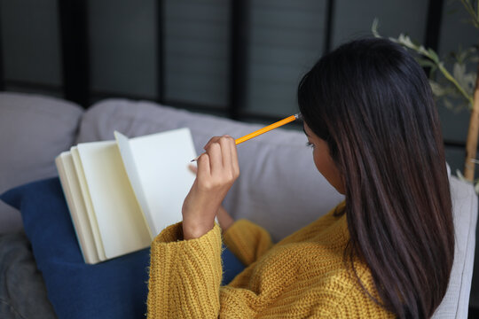 Relaxed woman sitting on the sofa reading and writing in a notebook
