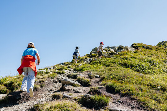 Children hiking up mountain trail on sunny summer day