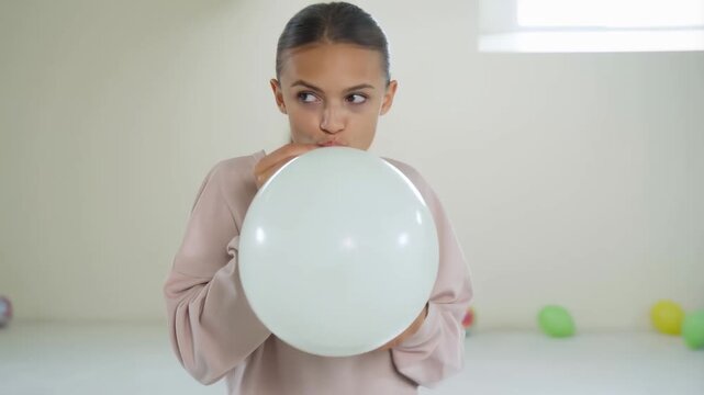 Teen girl inflating white balloon for party decoration indoor celebration concept