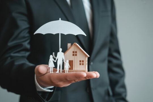 Businessman holding wooden house model with umbrella and family icon, symbolizing home insurance, property protection, financial security, and risk management for modern homeowners.